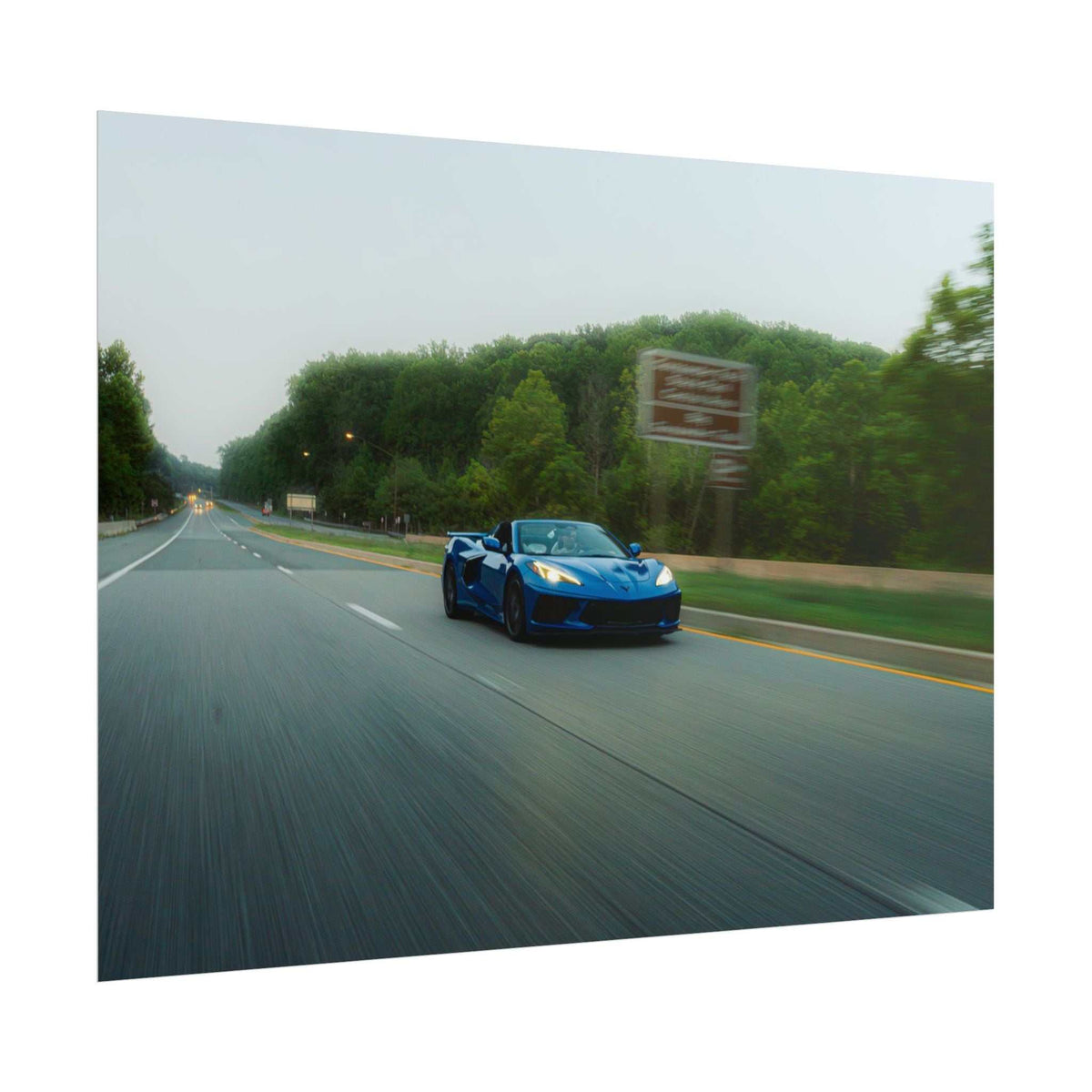C8 Corvette Stingray in blue driving fast on a tree-lined highway with motion blur capturing speed and depth
