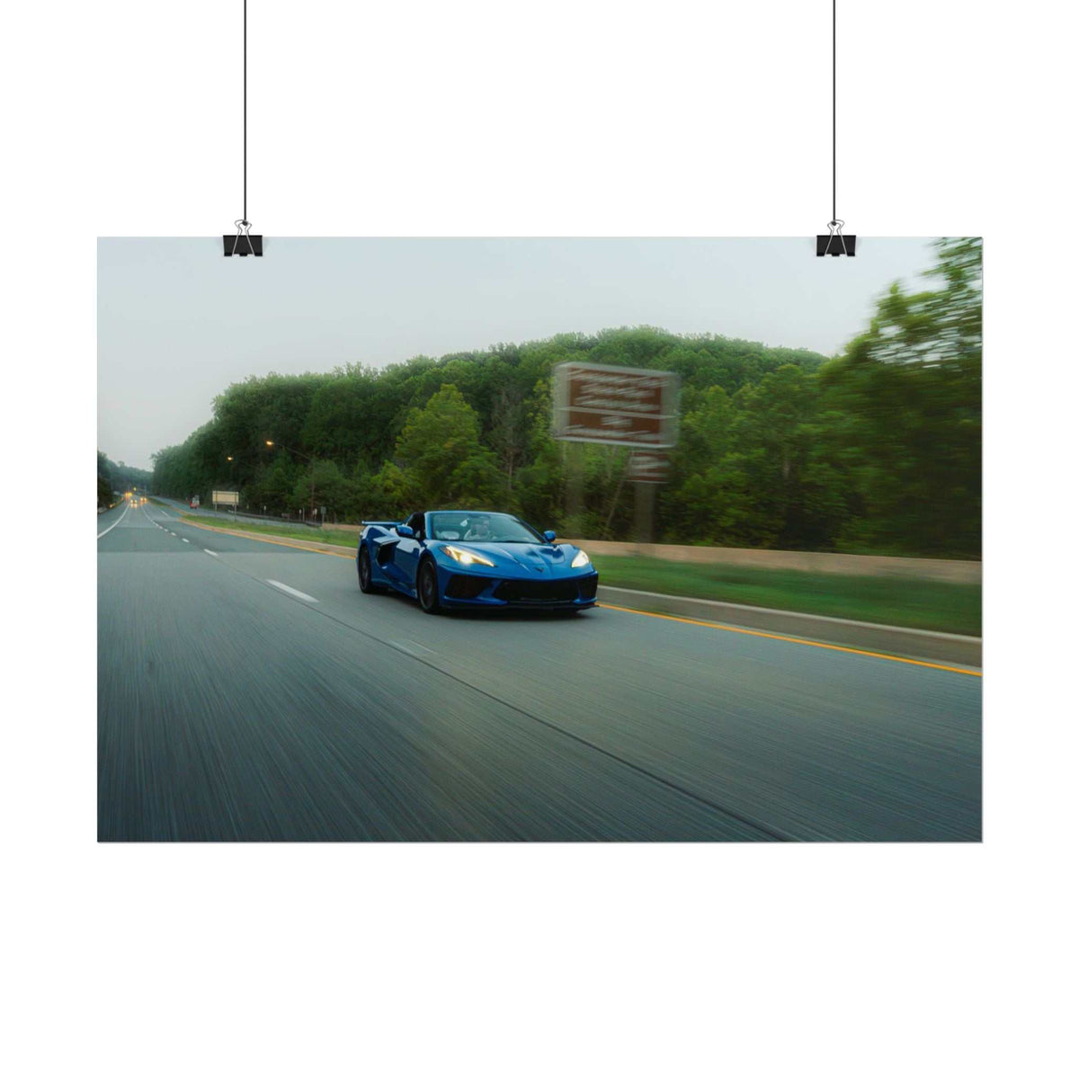 C8 Corvette Stingray blue sports car driving fast on a multi-lane road with motion blur and green trees in the background