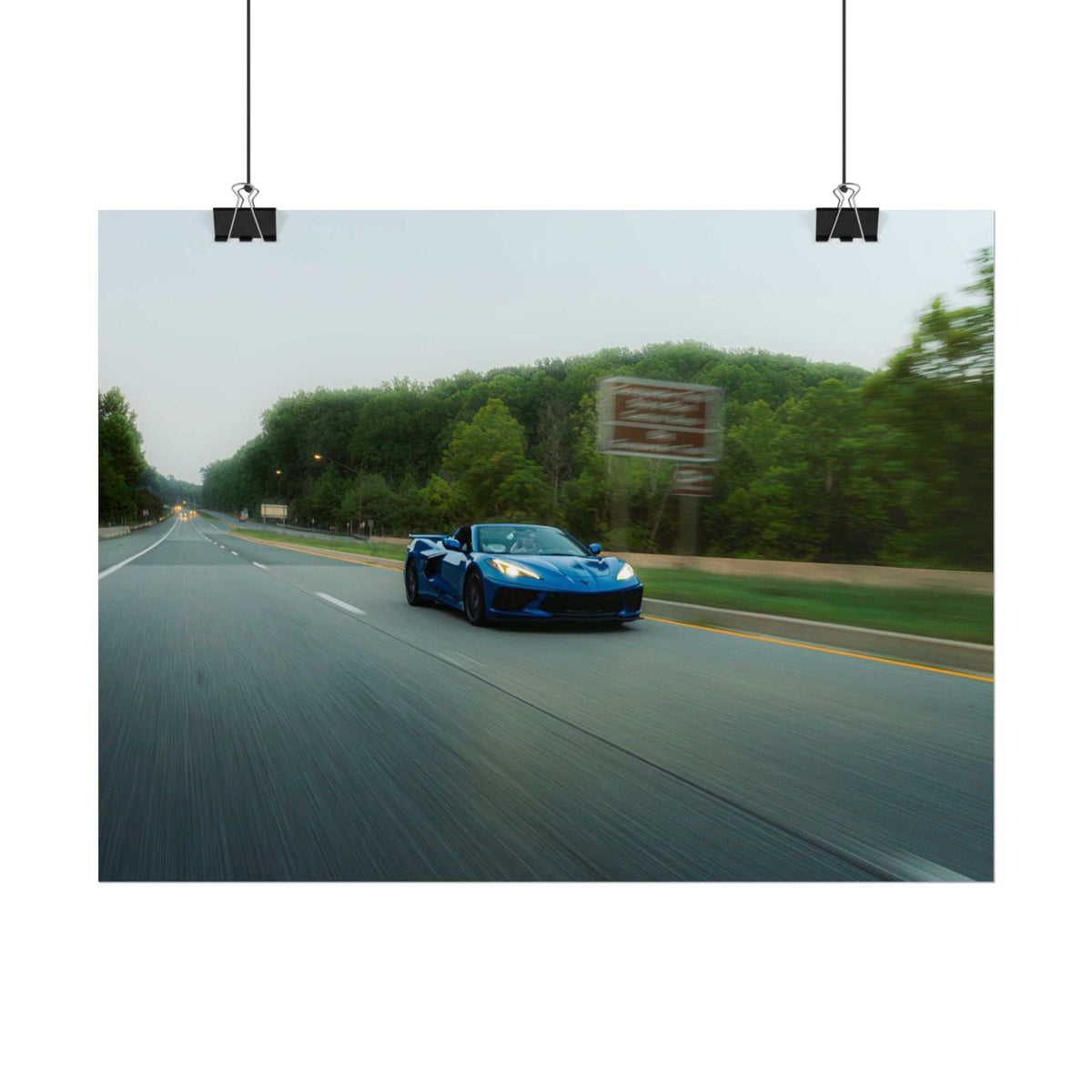 C8 Corvette Stingray blue sports car driving on tree-lined highway with motion blur and clear sharp detail