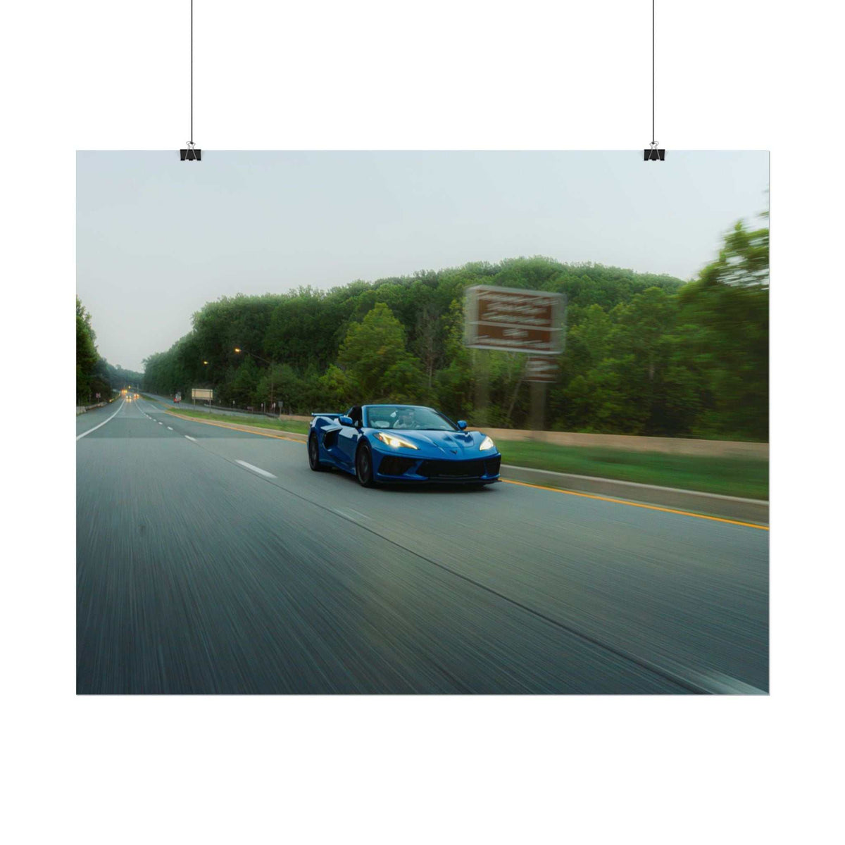 C8 Corvette Stingray blue sports car speeding on a highway with blurred motion and green trees along the roadside