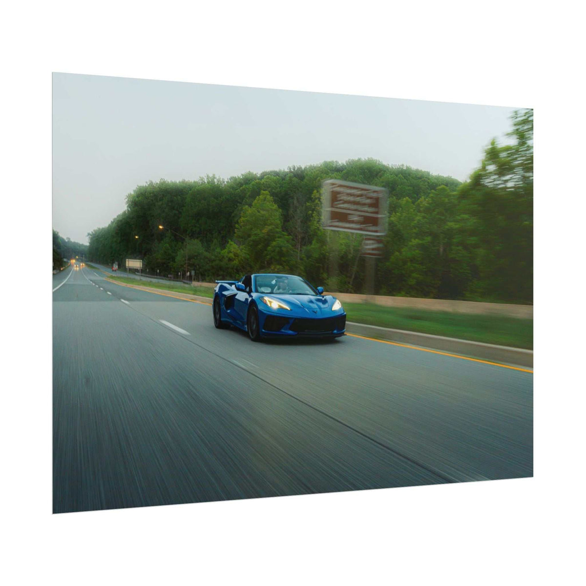 C8 Corvette Stingray blue sports car speeding on a highway with motion blur and green trees alongside the road