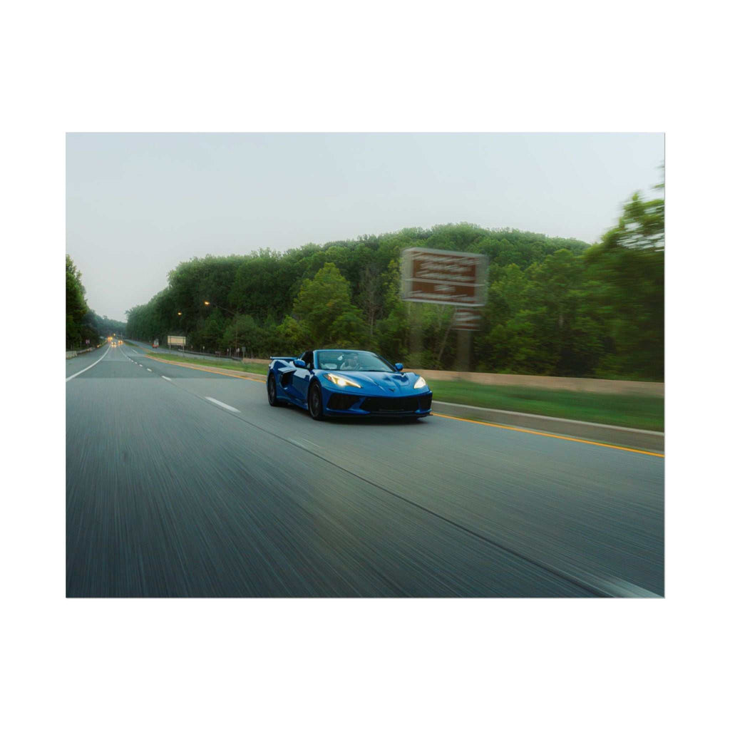 C8 Corvette Stingray blue sports car in motion on a highway with a blurred background of trees and road signs