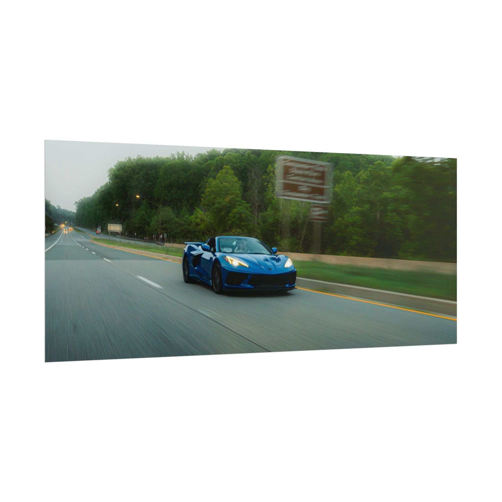 Blue C8 Corvette Stingray sports car driving on a tree-lined highway with motion blur capturing speed and depth