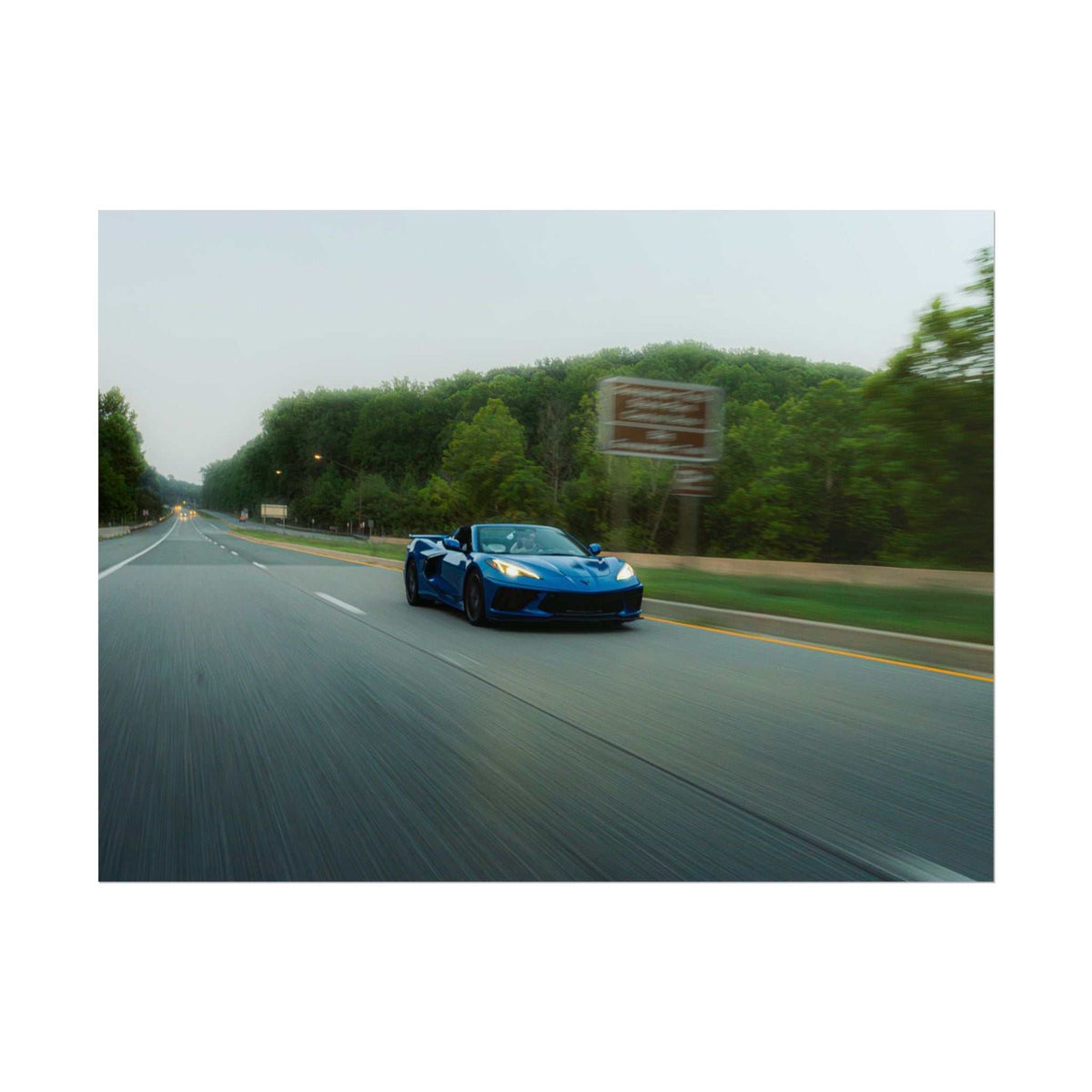 C8 Corvette Stingray in blue driving fast on highway with motion blur and green trees in background