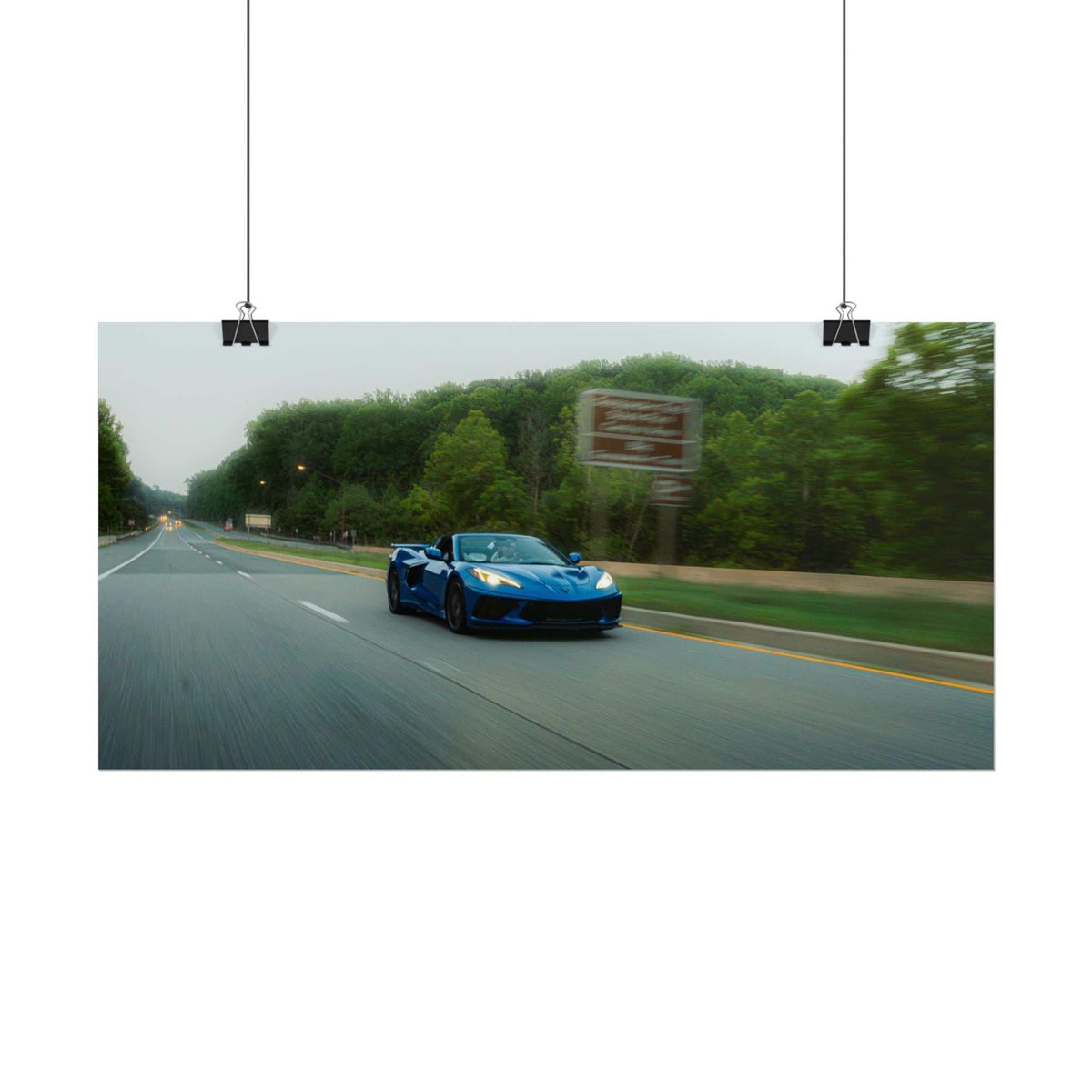 C8 Corvette Stingray blue sports car driving fast on highway with motion blur and tree-lined roadside