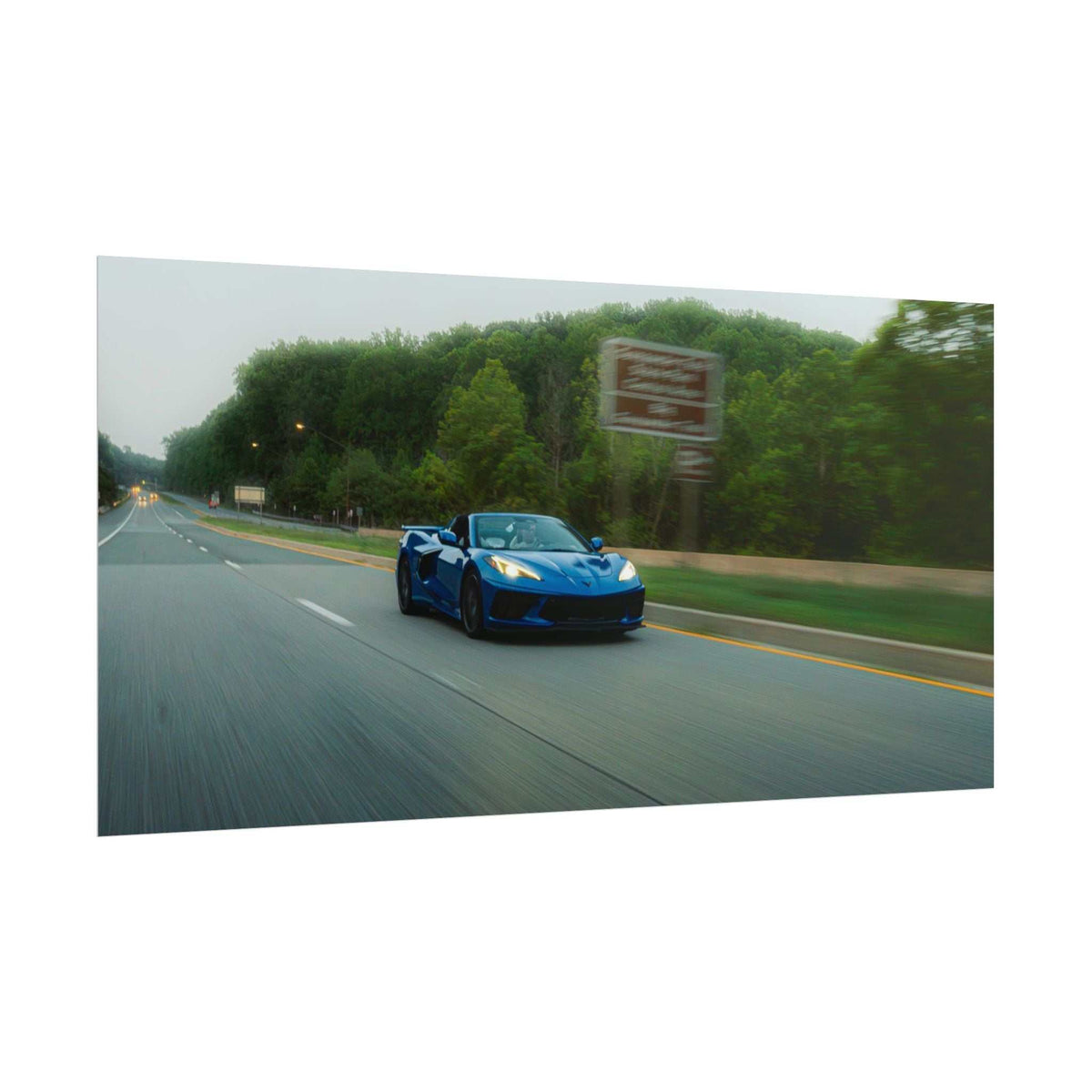 C8 Corvette Stingray blue sports car speeding on a highway with motion blur and green trees in the background