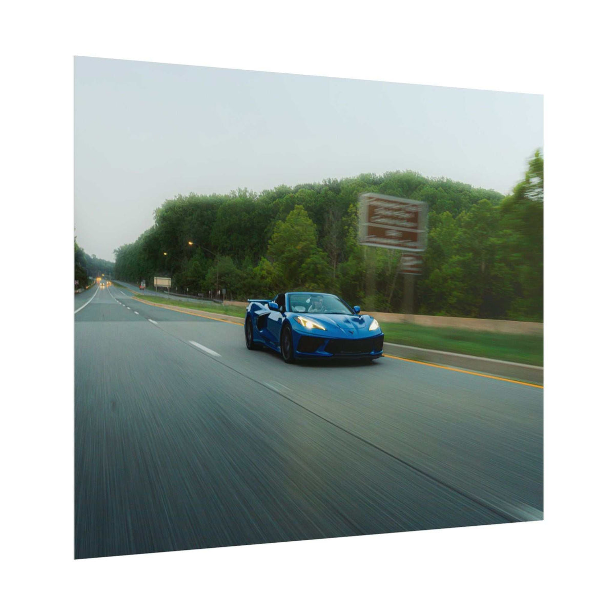 C8 Corvette Stingray blue sports car driving on tree-lined highway with motion blur effect and sharp design details