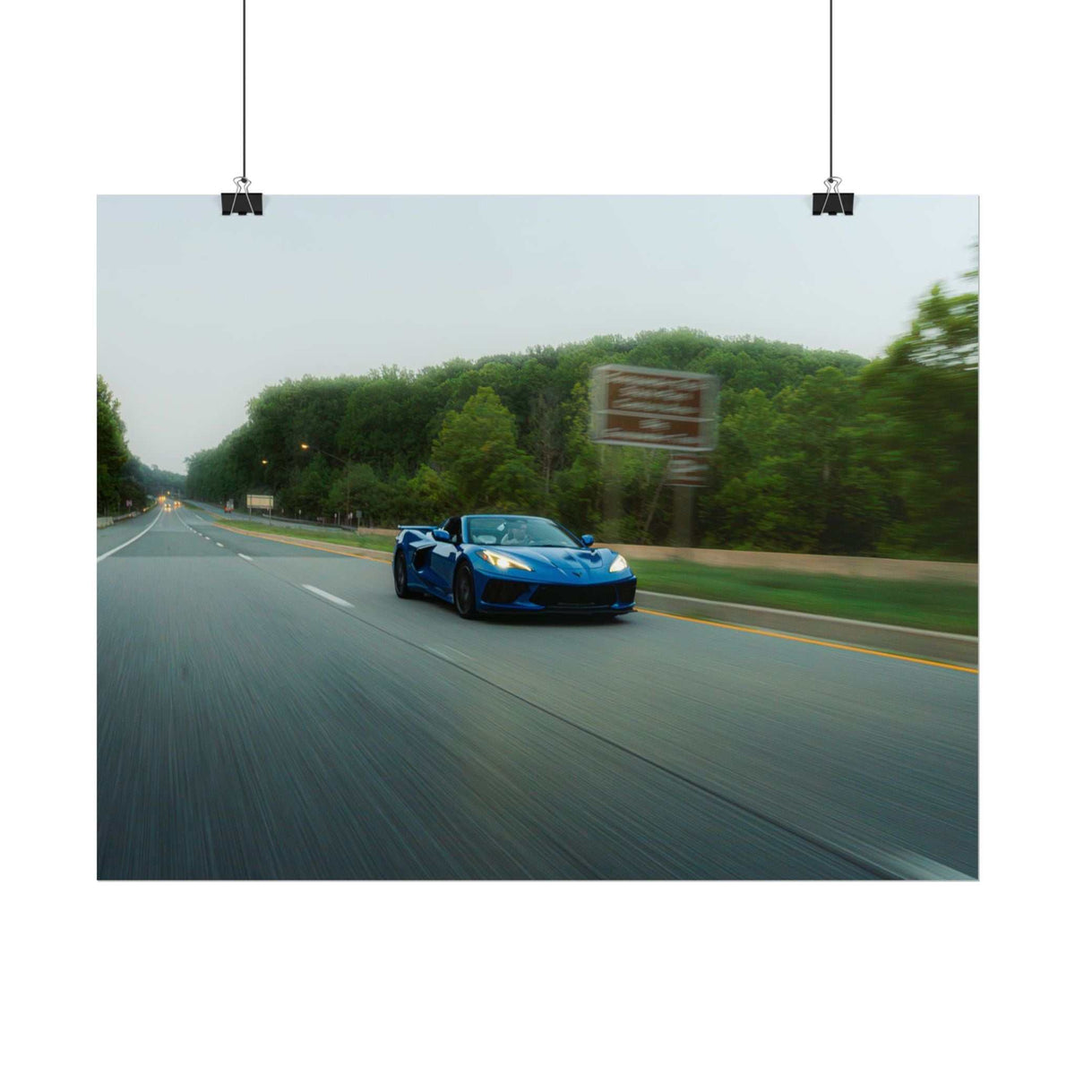 Blue C8 Corvette Stingray sports car driving fast on a tree-lined highway with motion blur and depth