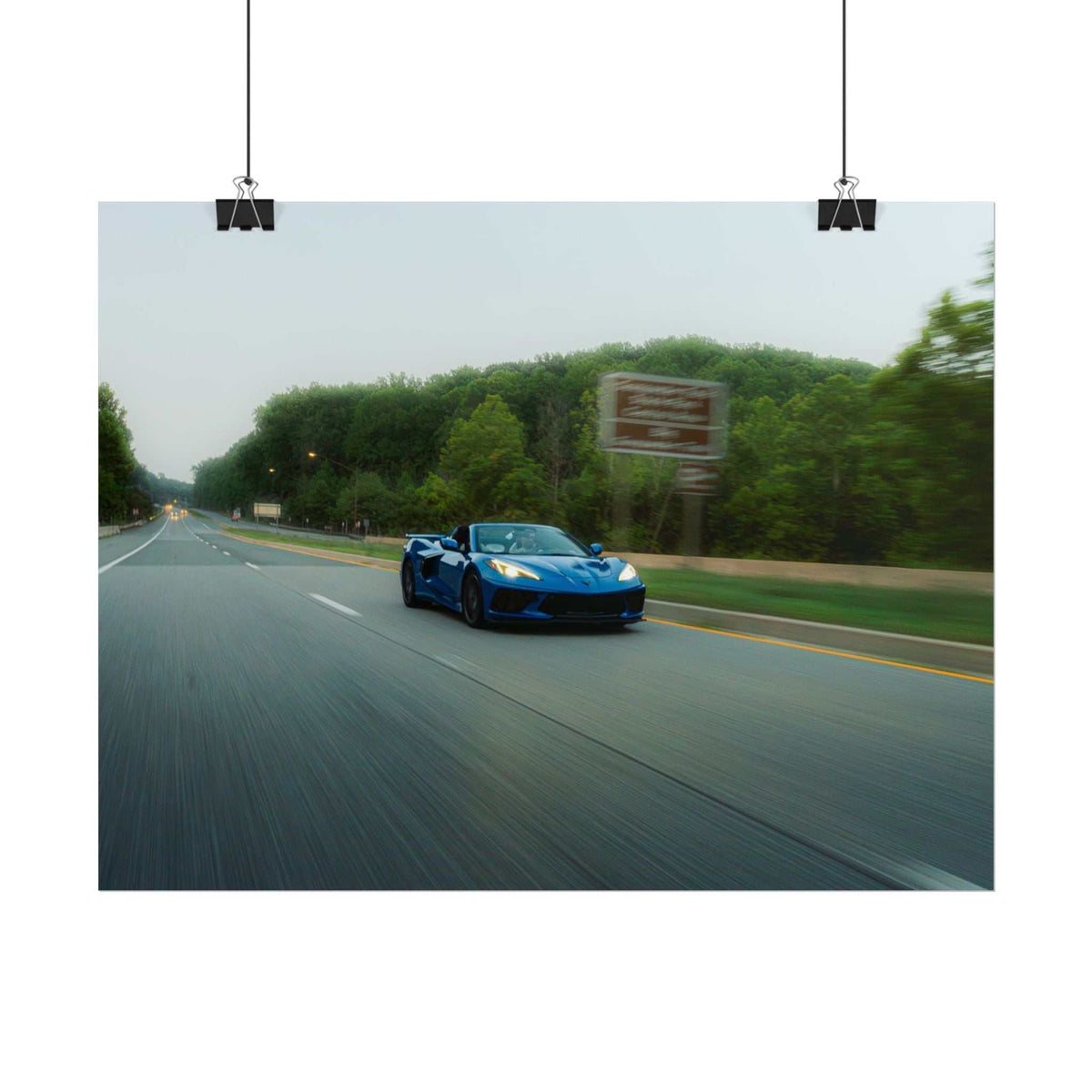 C8 Corvette Stingray blue sports car driving fast on tree-lined highway with motion blur and clear sky
