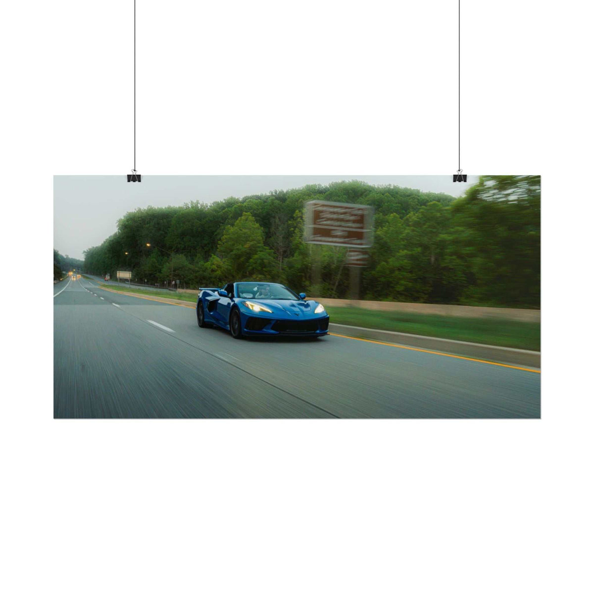 Blue C8 Corvette Stingray sports car in motion on a highway surrounded by green trees, showcasing dynamic speed and sleek design