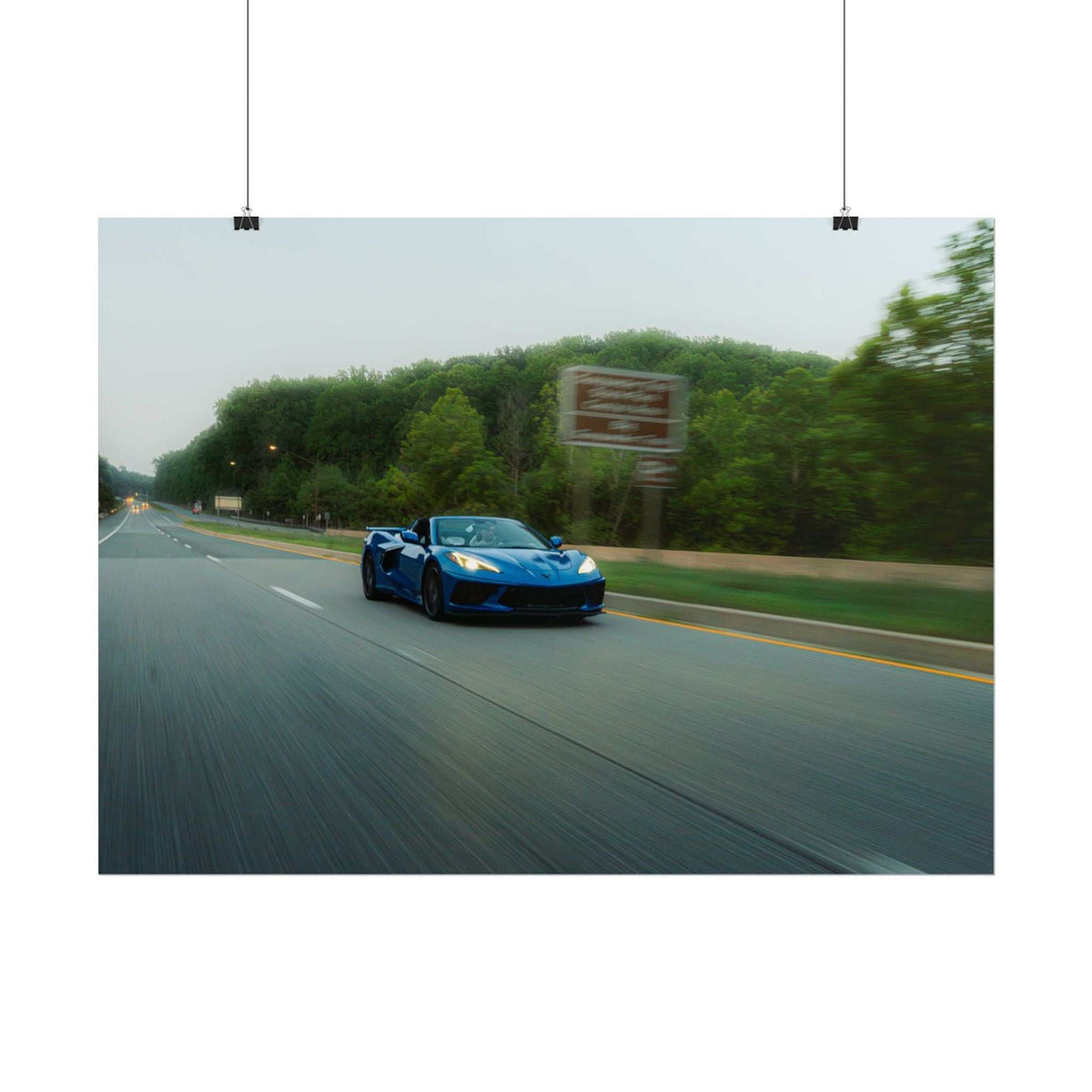 Blue C8 Corvette Stingray sports car in motion on a highway surrounded by greenery and speed blur