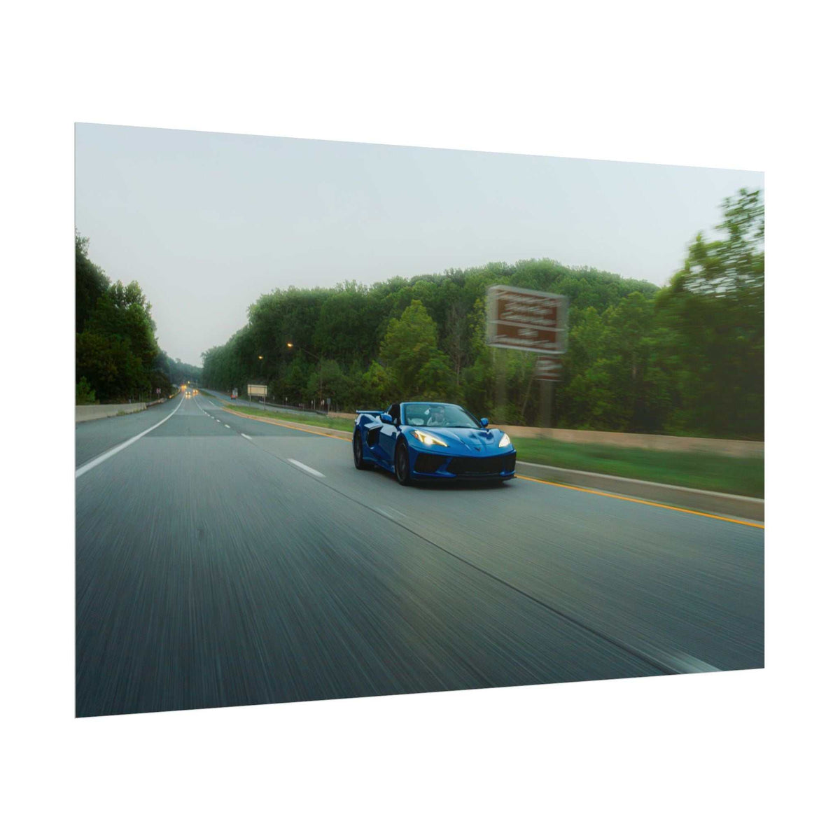 C8 Corvette Stingray blue sports car in motion on a tree-lined highway with motion blur and depth effect