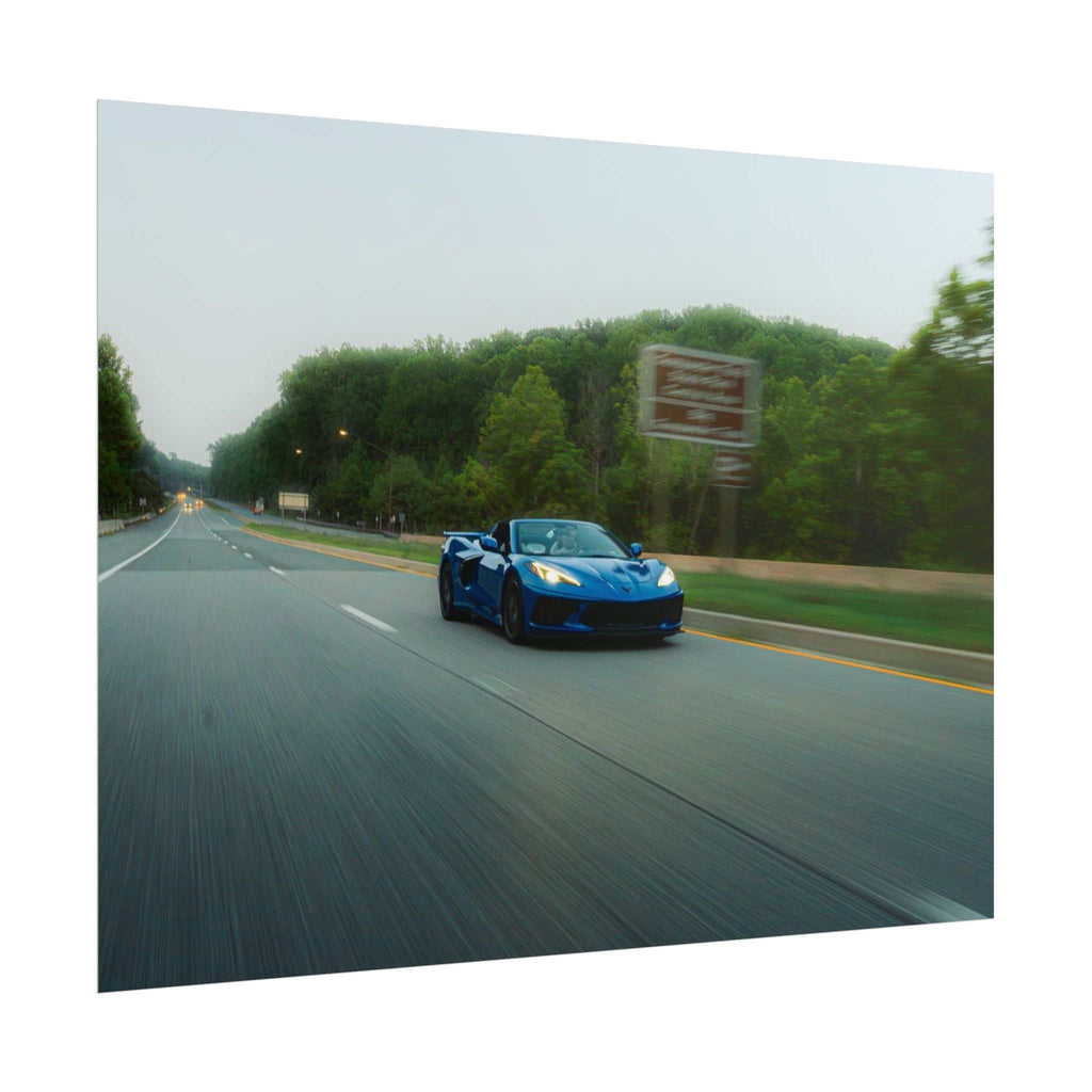 Blue C8 Corvette Stingray sports car in motion on a tree-lined highway with speed blur effect capturing dynamic movement
