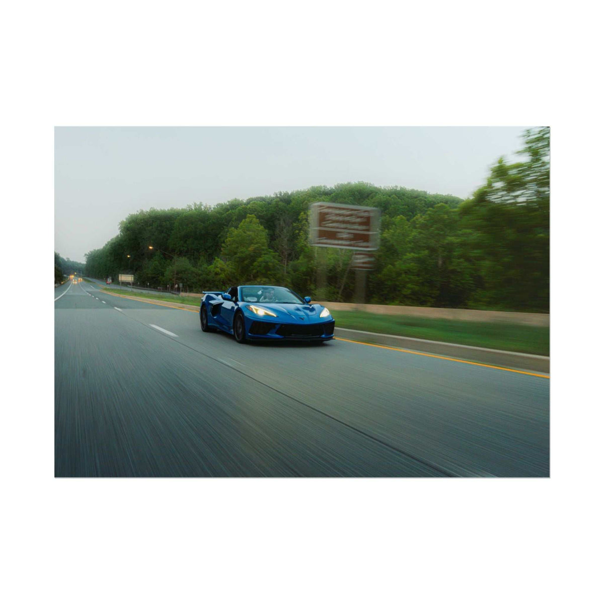 C8 Corvette Stingray blue sports car driving fast on a tree-lined highway with motion blur and clear road markings
