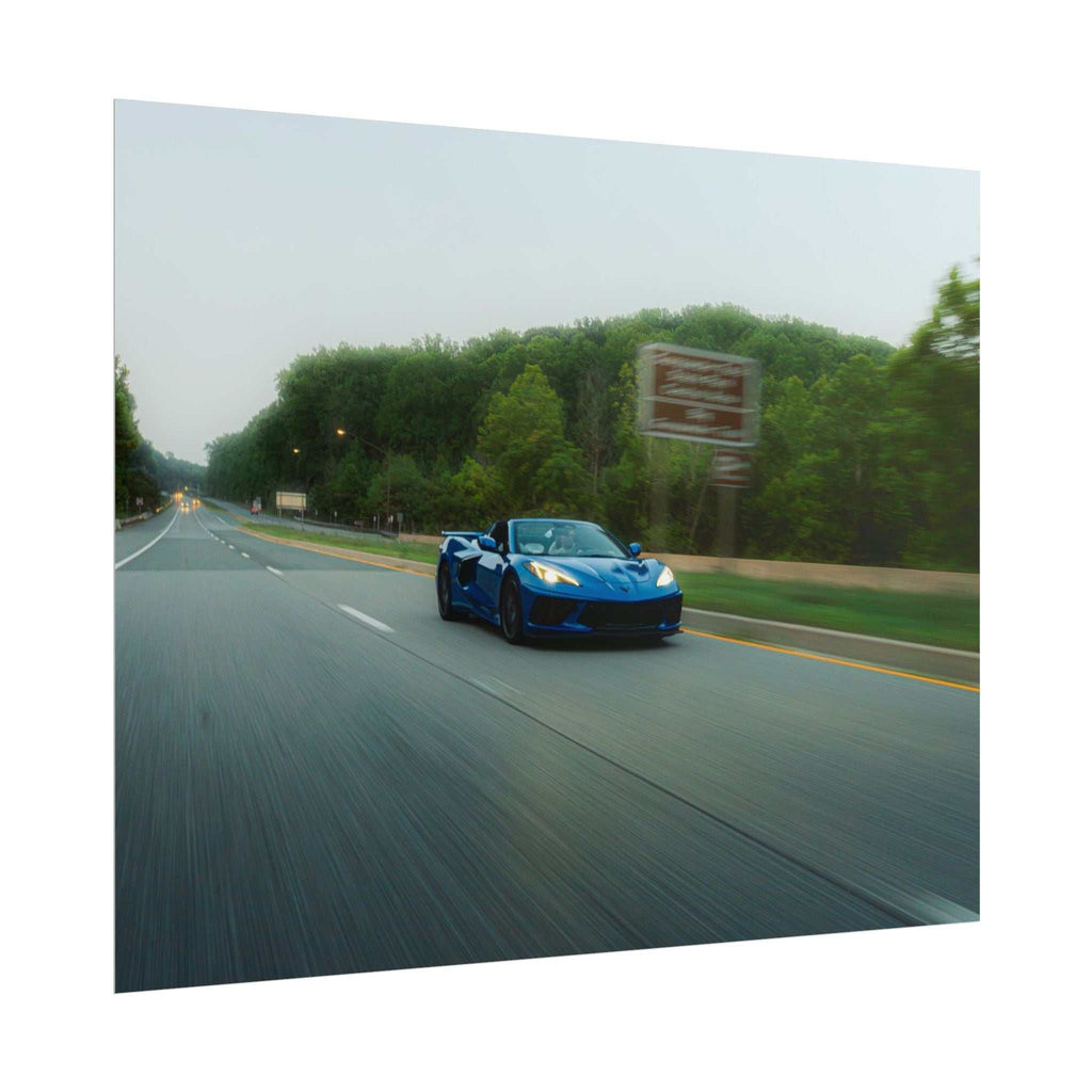 C8 Corvette Stingray blue sports car in motion on a highway with blurred road and green trees alongside
