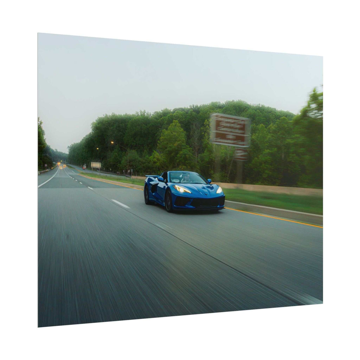 C8 Corvette Stingray blue sports car in motion on a highway with blurred road and green trees alongside