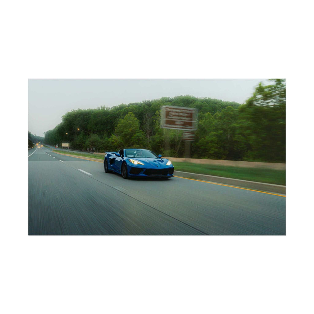 C8 Corvette Stingray blue sports car speeding on a highway with blurred road and green trees in the background