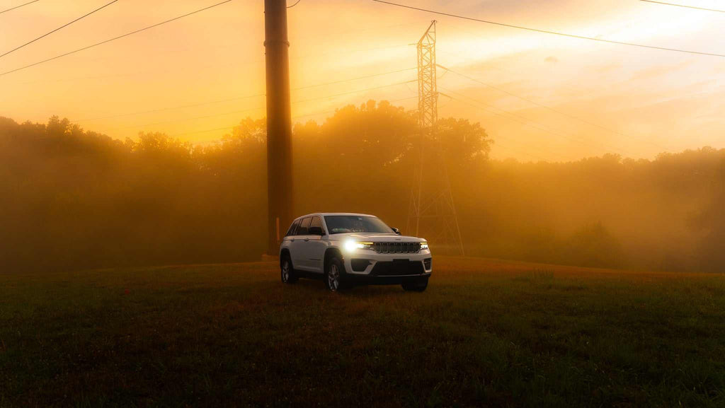 White SUV with headlights on in a grassy field at sunset with fog and orange hues using Dreamy Glow Lightroom Preset