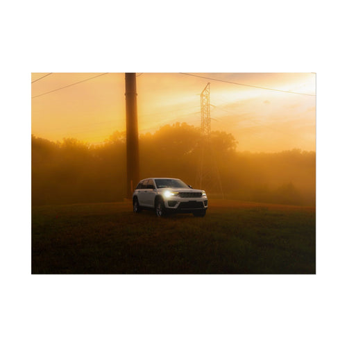 Jeep Grand Cherokee in silver cutting through warm, foggy sunset landscape with visible headlights and power lines