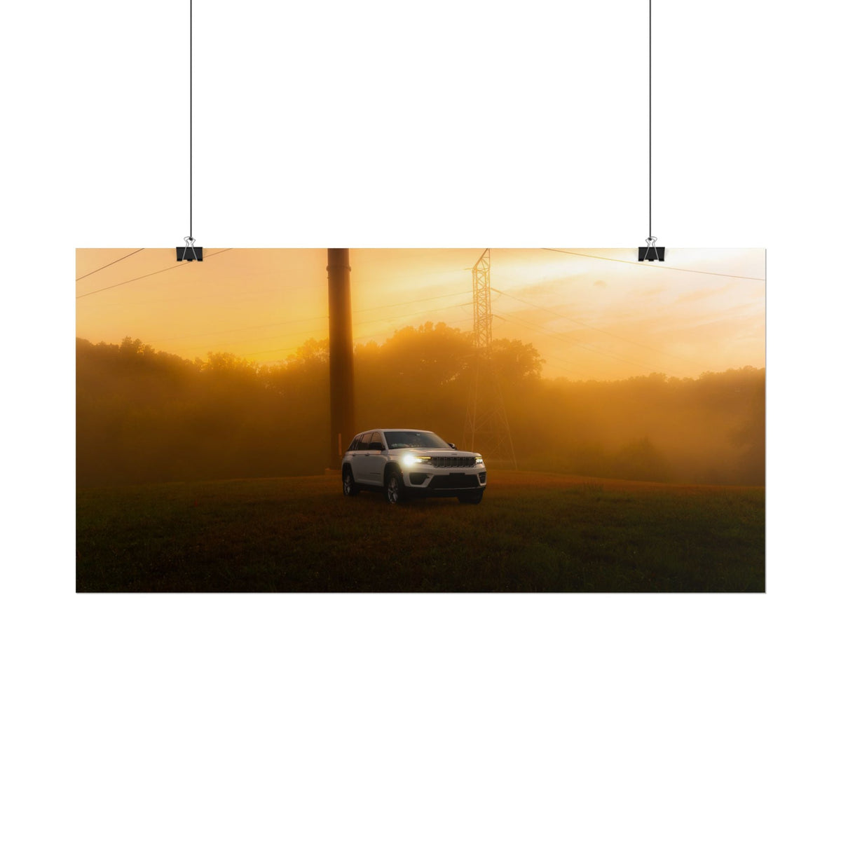 Jeep Grand Cherokee in silver metallic color driving through warm sunset fog with glowing headlights and power lines in background