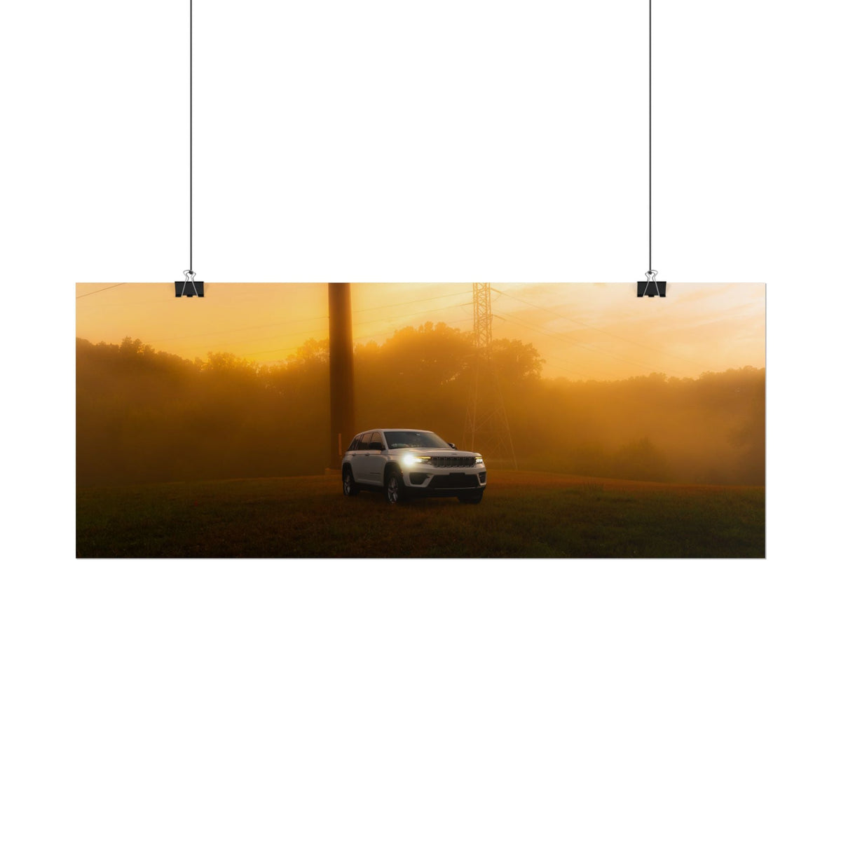 Jeep Grand Cherokee in white cutting through a warm, hazy amber sunset fog with headlights glowing and power lines in background