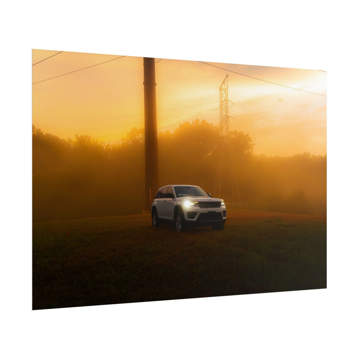 Jeep Grand Cherokee in white with headlights on cutting through hazy, warm orange sunset fog in a rural setting