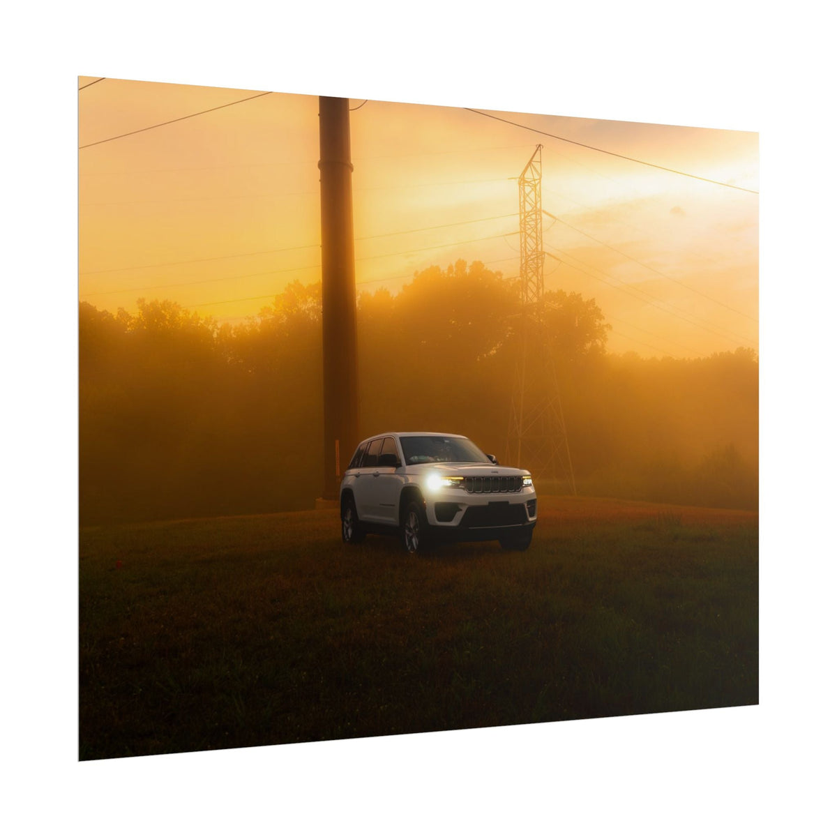 Jeep Grand Cherokee white SUV with headlights on in warm, hazy sunset fog among power lines and trees