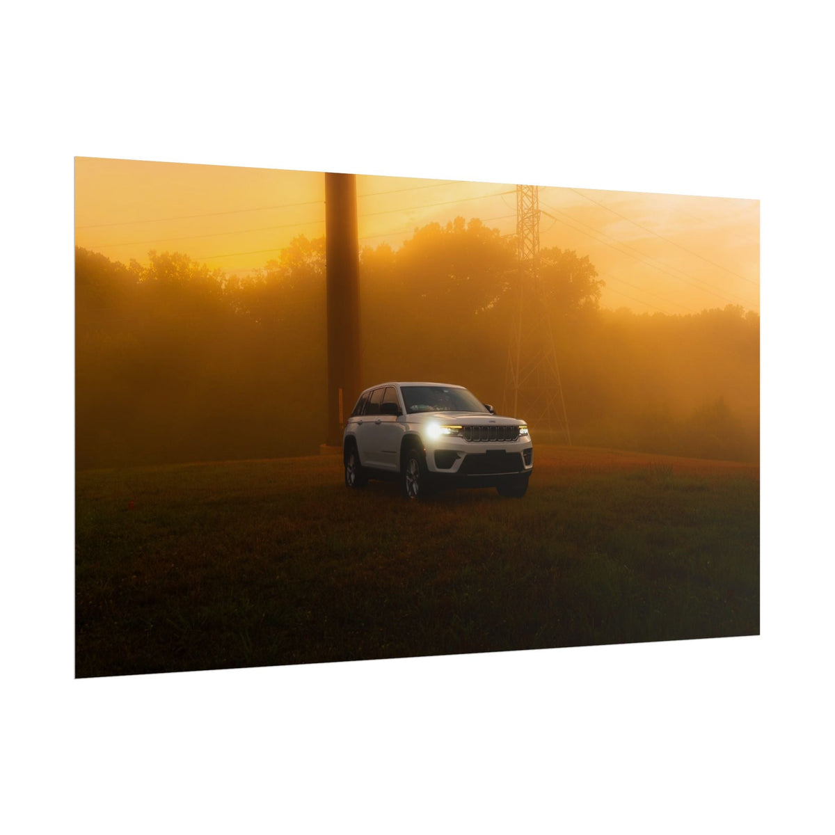 Jeep Grand Cherokee white SUV with headlights on parked on grassy field in warm hazy sunset fog with power lines