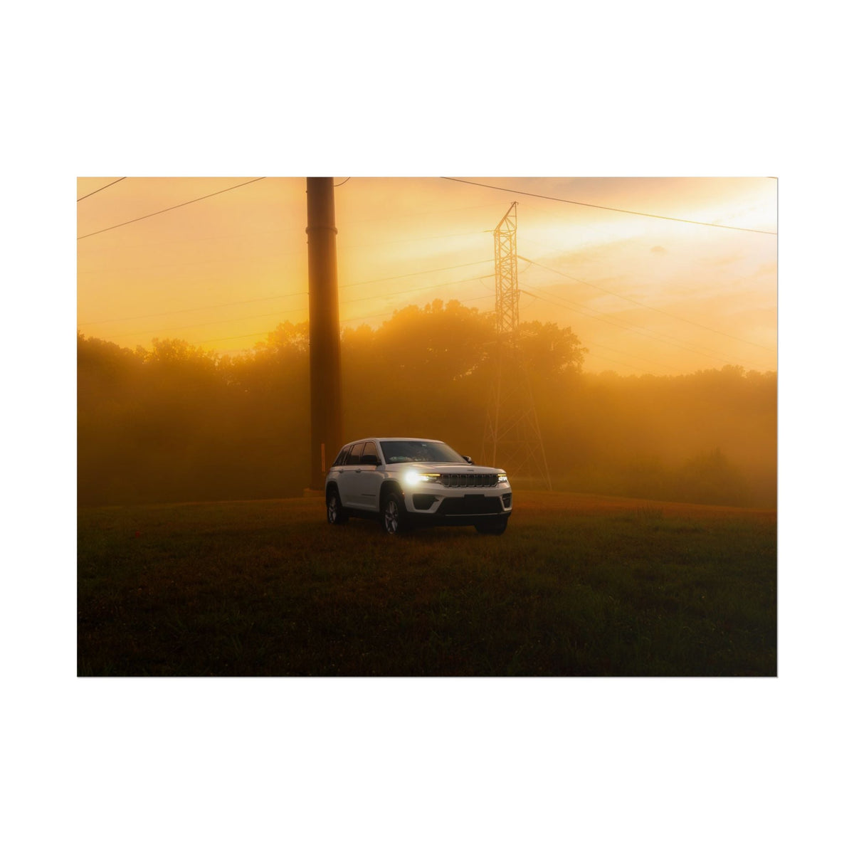 Jeep Grand Cherokee white SUV with headlights on driving through warm orange sunset fog with power lines and trees